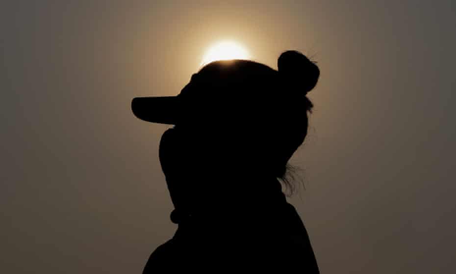 silhouette of woman in cap and mask against orange sky