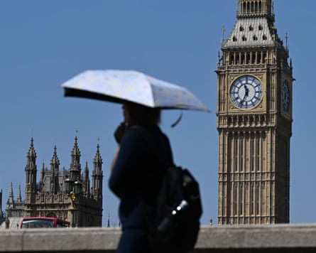 A person using an umbrella as a sunshade in front of the houses of parliament