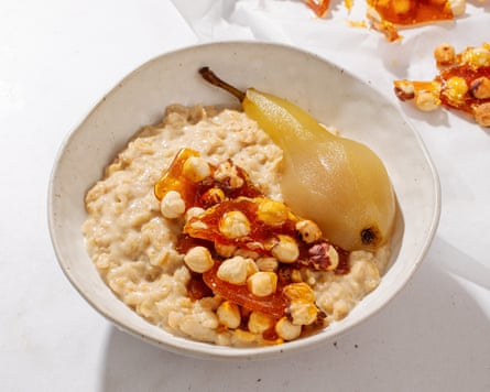 An artfully presented bowl of porridge topped with honey, nuts and a whole poached pear