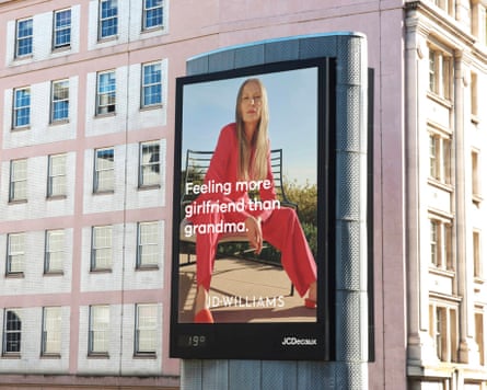 A very large advert on the side of a building shows an older women in a bright red/pink suit while siting on a seat