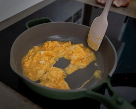 Our Place pan with scrambled eggs cooking and being stirred by a silicone spatula