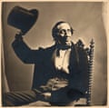 An old sepia-toned image of a man sitting on an ornate chair wearing 19th-century clothing, and holding up his top hat