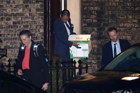 A police officer exits the London residence with boxes.