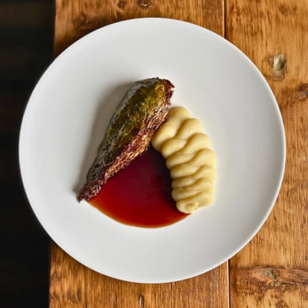 A wedge of roasted cabbage with swirls of potato puree and a red-brown gravy on a white plate