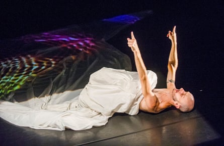 Mark in a white sheet, pointing towards the ceiling, with coloured lights on the stage