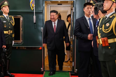 Kim Jong-un smiles as he stops off a train with aides standing nearby and paramilitary police officers standing to attention