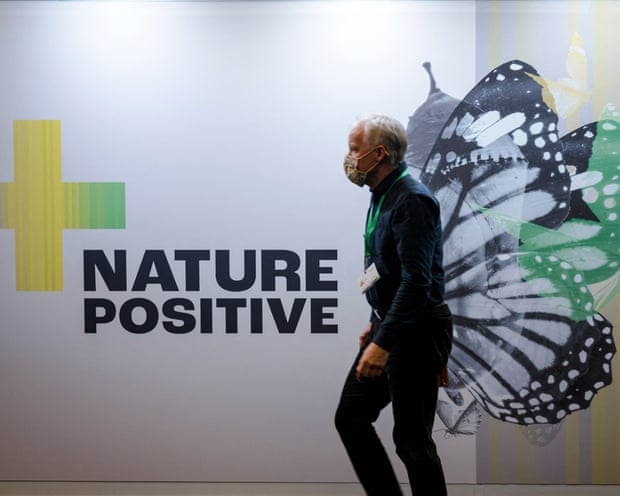 A man wearing a facemask passes a billboard that reads 'Nature Positive'. The picture of a butterfly on the billboard makes it look as though the man has wings.