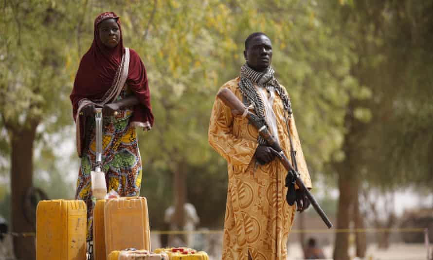 A member of a civilian vigilante group holds a hunting rifle while a woman pumps water into jerrycans in Kerawa, on the border with Nigeria in the far north of Cameroon 16 March 2016.