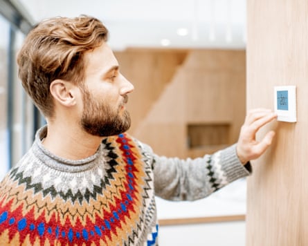 Man in sweater feeling cold adjusting room temperature with electronic thermostat