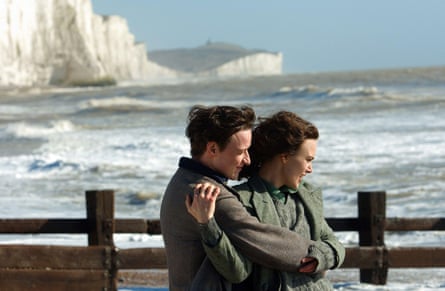 They hold each other while standing by a fence at the sea