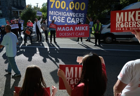 Two lines of people holding political signs cast long shadows on a street.
