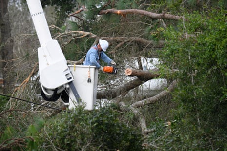 man in blue shirt and white hard hat works to clear tree limbs while in a lift