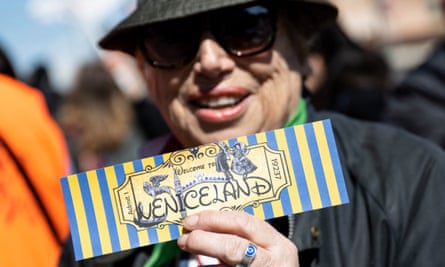 A woman in sunhat and glasses holding a ticket reading ‘Welcome to Veniceland’.