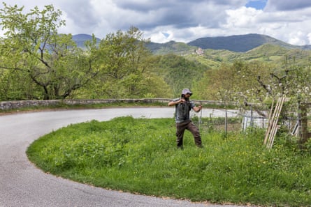 A man stands with a fishing rod in undergrowth at the side of a country road