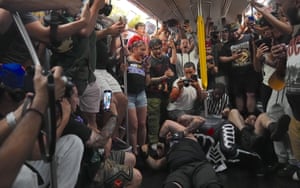 People crowd around in the train carriage as wrestlers grapple on the floor