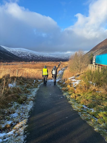 John Kuei and Giel Malual walk along a road in Scotland with snowy mountains visible in the distance.