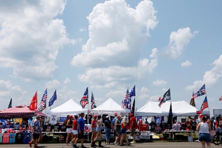 A large crowd and vendors under tents at a Trump rally with flags flying.