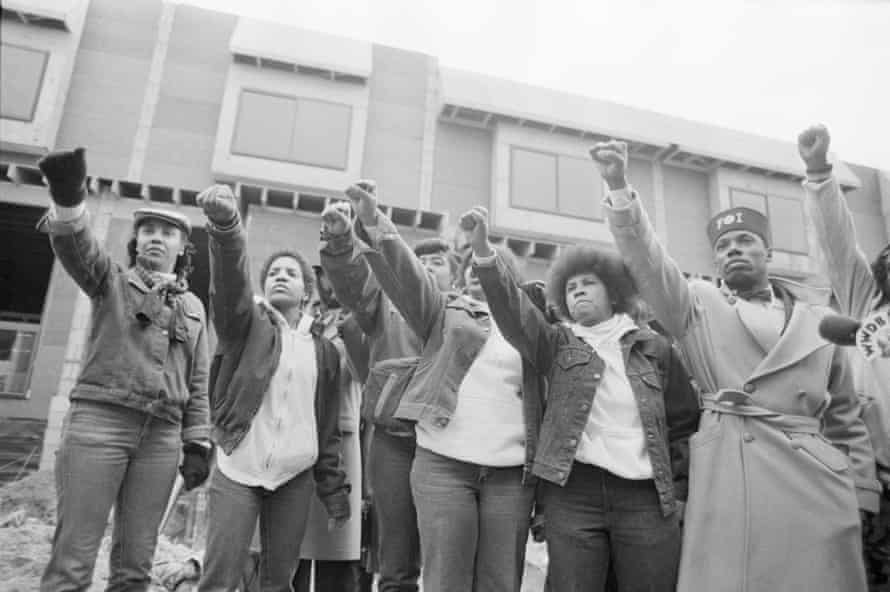 Mourners of MOVE members killed in the bombing by the Philadelphia Police stand in front of their former headquarters. They raise their arms with the Black Power salute as the funeral procession for leader John Africa passes.