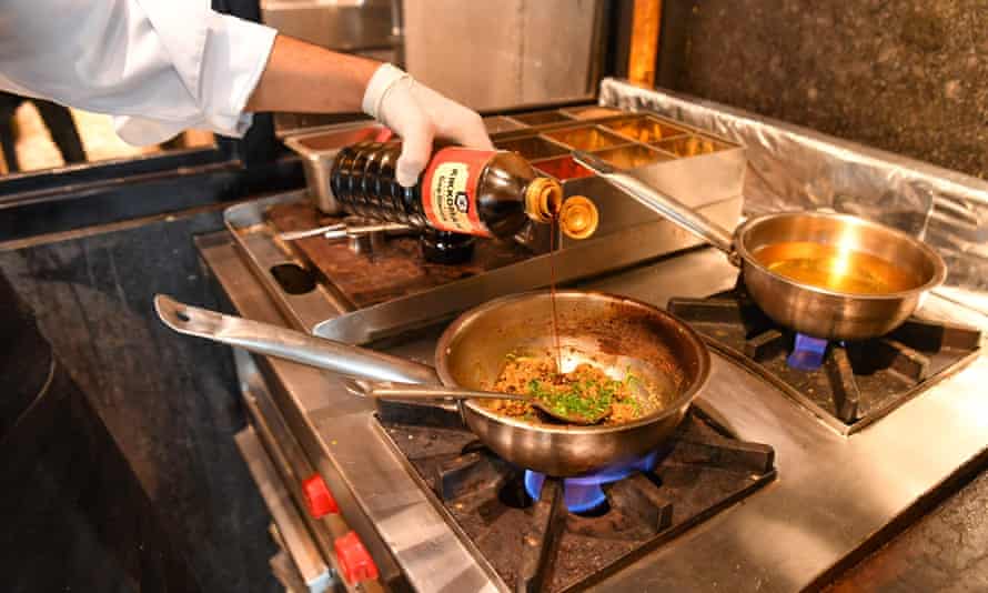 A chef seasoning a dish with soy sauce as it cooks