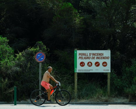 A cyclist rides past a sign warning of the risk of fire in El Saler Natural Park, amidst an extreme heat warning in Valencia, Spain.