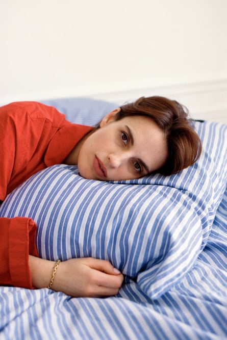 A woman wearing an orange shirt rests her head on a blue-striped pillow in bed