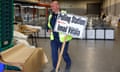 Man in a hi-vis jacket in a warehouse carries a polling station sign