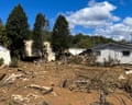 A muddy field strewn with debris, a house and barn in the background