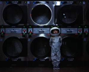 A girl in an astronaut costumes stands in a laundromat