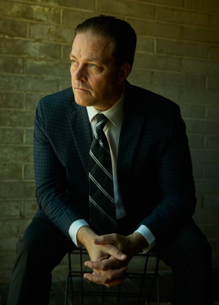A man in a suit sits with hands in front of him.