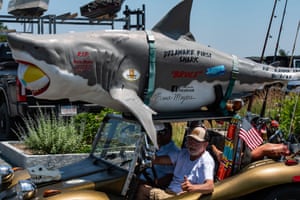 A great white shark with a beach ball in its mouth and ‘Delaware First Shark’ and ‘Bruce’ written on its side is driven around atop a dune buggy