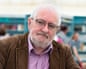 Terry Eagleton, an older man with white hair and beard, wears a brown jacket and lilac shirt