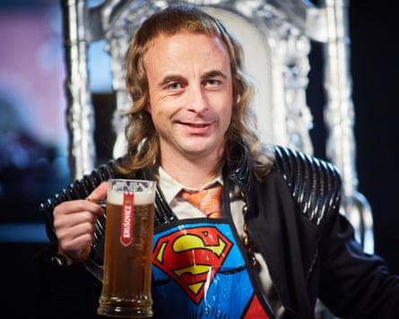 Paul Foot holding a pint of beer and wearing a Superman emblem over a black jacket