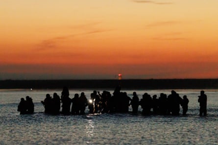 People standing waist-deep in the sea, silhouetted against the sunset.