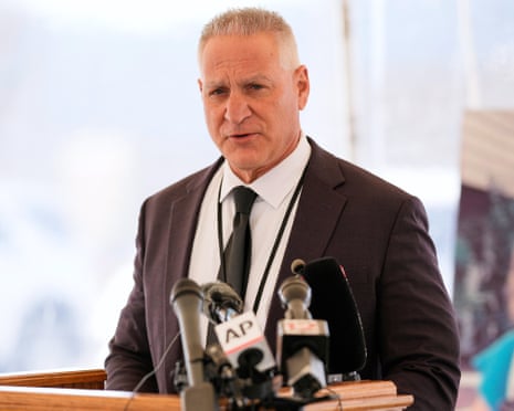 A man in a suit speaking at a lectern in front of a bank of microphones.