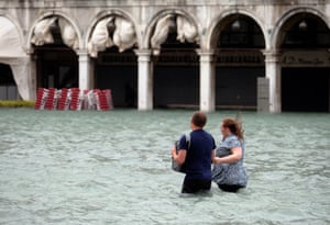 A couple walk in the flooded Saint Mark Square during a period of seasonal high water in Venice