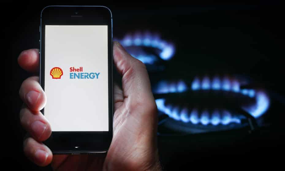 A man looking at the website logo for energy company Shell Energy (formerly First Utility) on his phone in front of a gas cooker