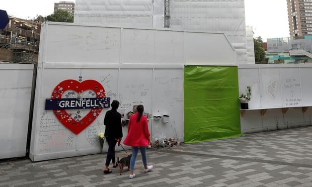 Women walk past a hoarding covered in messages of condolence at the base of Grenfell Tower