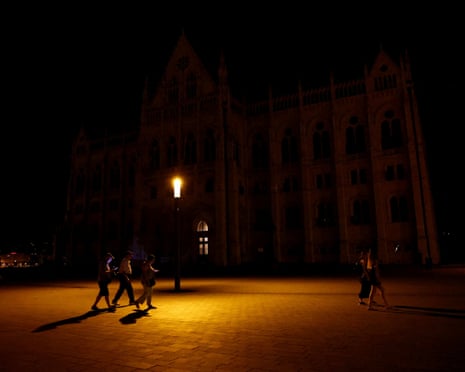 People walk next to the parliament building as lights are turned off at Budapest landmarks to reduce energy due to a power crisis in Budapest, Hungary.
