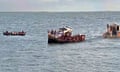 A naval patrol boat is seen close to two overloaded boats full of people on a wide river.