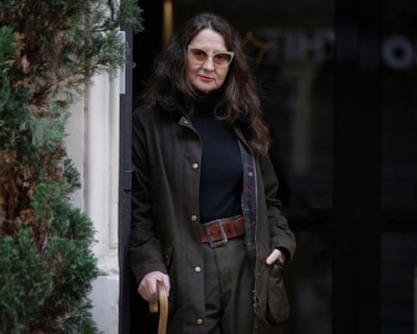 Lucrecia Martel standing in a doorway wearing dark clothes and sunglasses and holding a walking stick