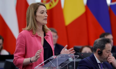 Roberta Metsola wearing a pink jacket standing at a lecturn