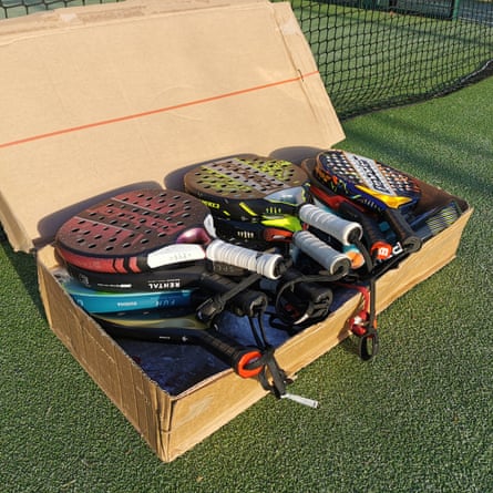 Padel racket Group Shot. The rackets are piled into a cardboard box lying on the green padel court.