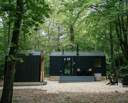 Black wooden cabins with chimneys in a clearing in a wood.