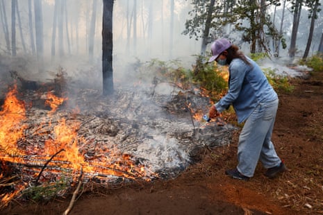 A woman dousing flames in a forest.