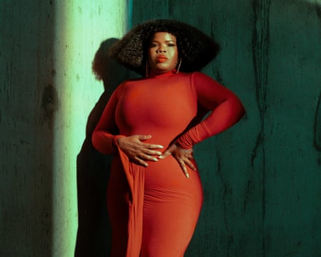 Danielle Ponder poses in a red dress against a teal wall