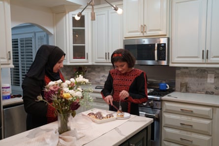 A mother and daughter stand at a kitchen island that has a vase of flowers on it. The daughter is serving herself a dessert