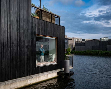 Philip van der Wees, photographed from outside him home, looks out from a large square window at the water