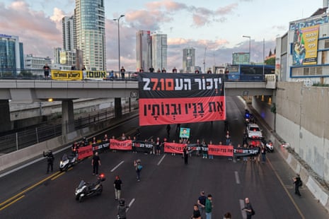 A large banner displayed on a bridge over a road blocked by protesters.