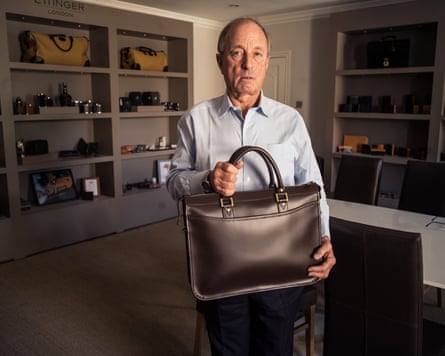 Robert Ettinger holds a brown leather briefcase in the Ettinger showroom lined with leather goods