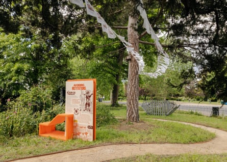 A path curves around a tree, in a green garden with an orange art exhibit.